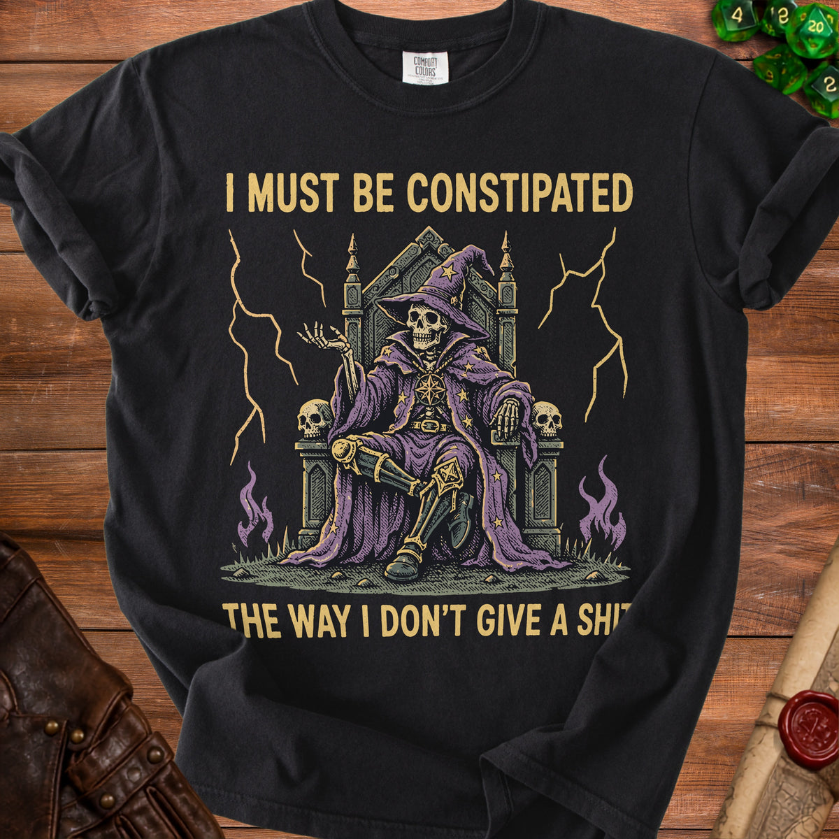 Black t-shirt with skeleton wizard sitting on a throne, text reads "I MUST BE CONSTIPATED THE WAY I DON'T GIVE A SHI".