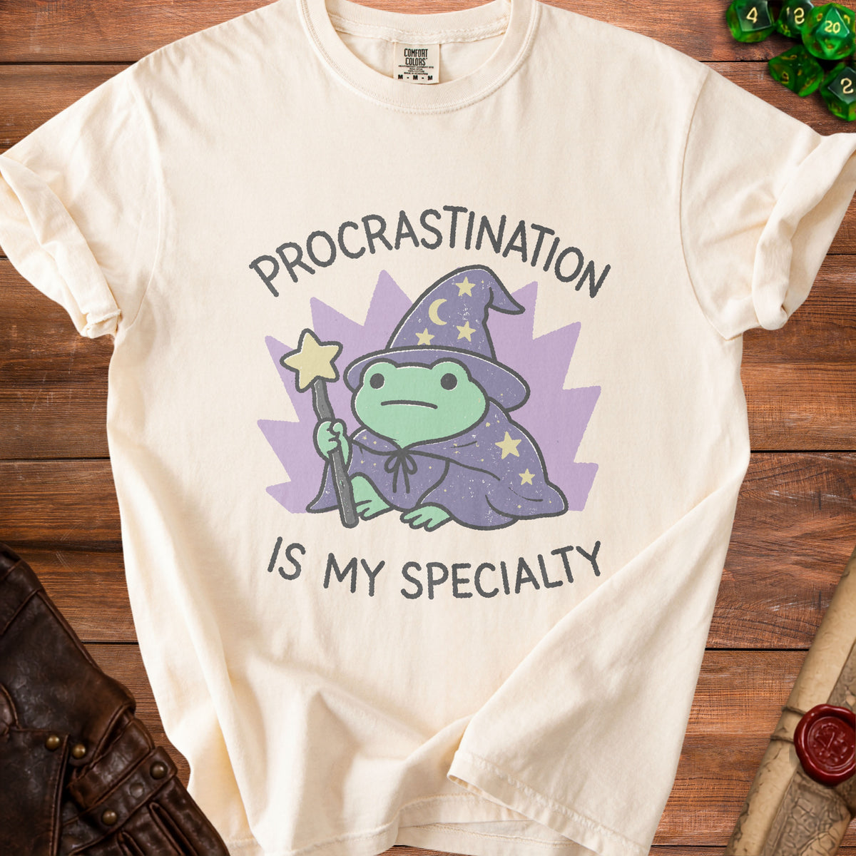 Cream t-shirt with a frog wizard graphic and text "PROCRASTINATION IS MY SPECIALTY".