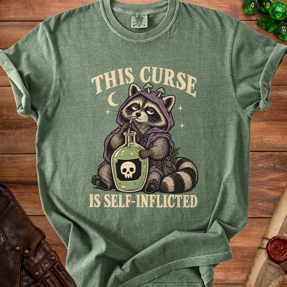 Green t-shirt with a raccoon in a hooded robe holding a potion bottle that says "THIS CURSE IS SELF-INFLICTED".