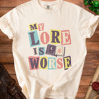 Cream t-shirt with "MY LORE IS WORSE" in colorful, cutout block letters.
