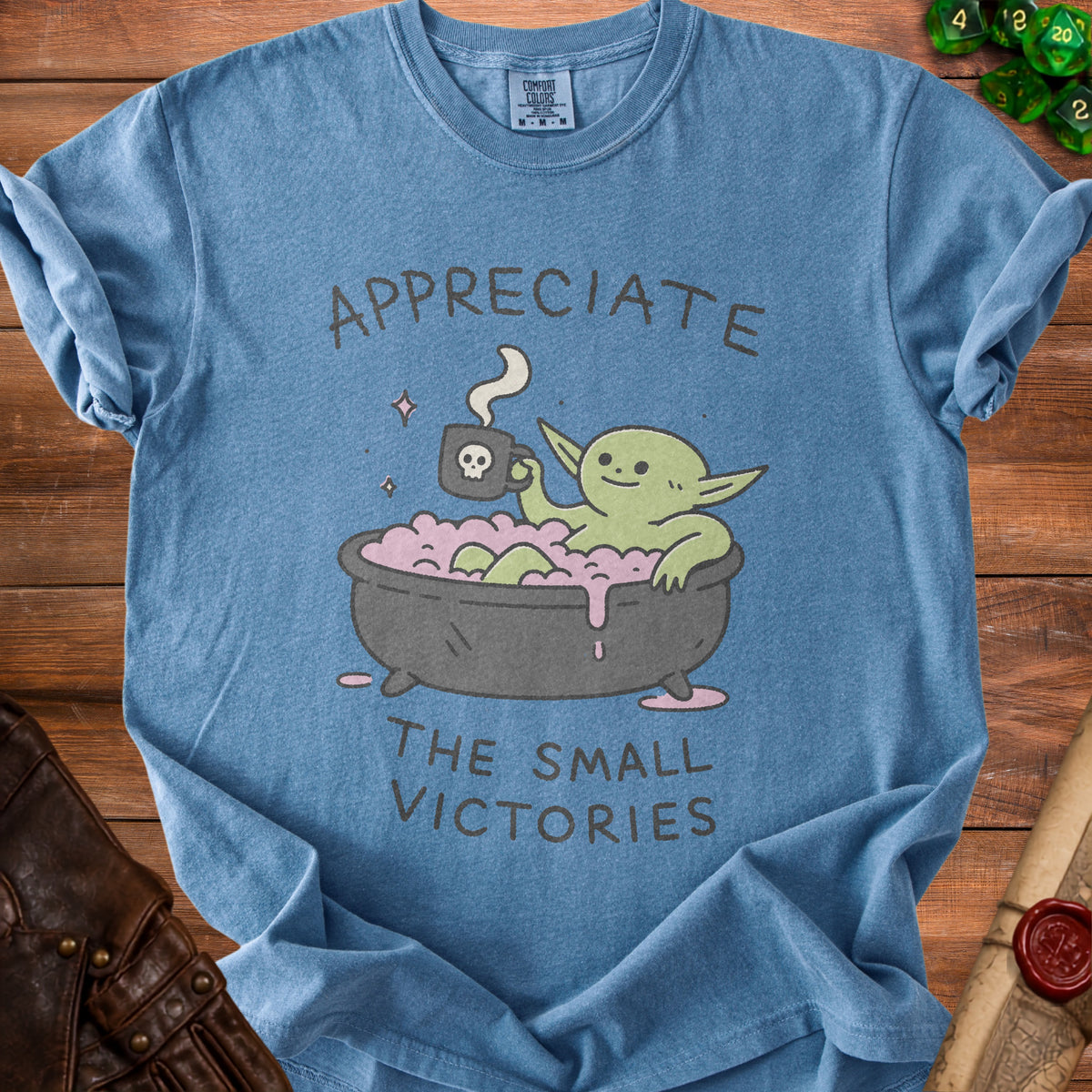Blue t-shirt with illustration of creature in bathtub holding skull mug.