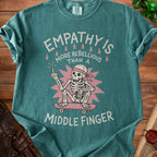 Teal Comfort Colors t-shirt with skeleton on skateboard and text "EMPATHY IS MORE REBELLIOUS THAN A MIDDLE FINGER".