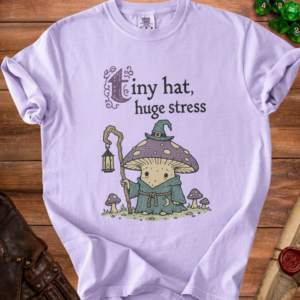 Lavender t-shirt with cartoon mushroom wearing a hat, holding a lantern, and text "Tiny hat, huge stress".