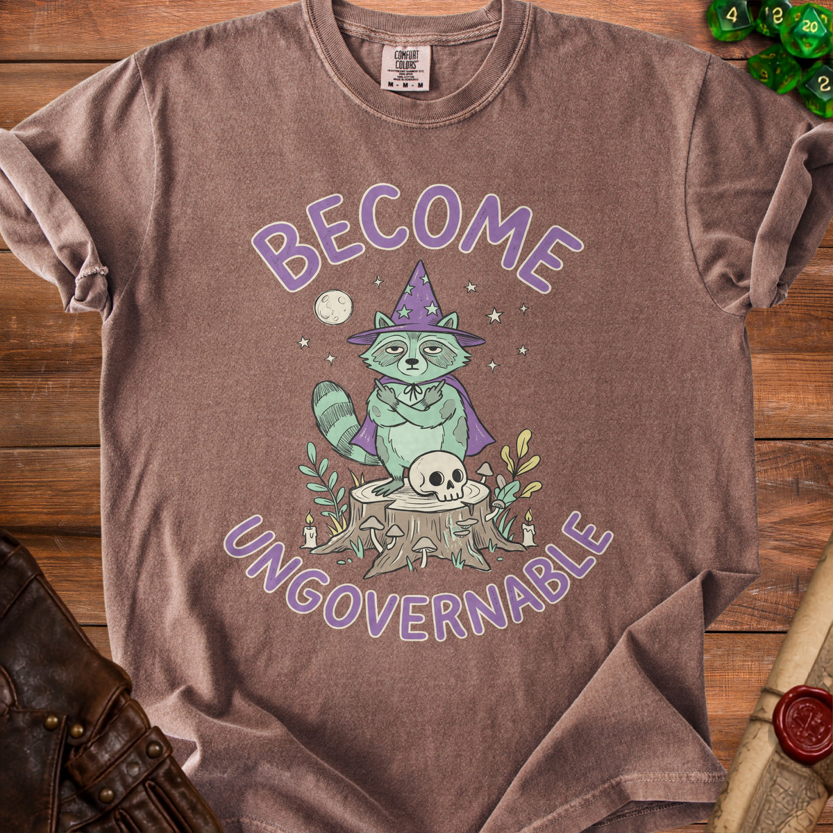Brown t-shirt with purple text "BECOME UNGOVERNABLE" and cartoon raccoon wizard graphic.