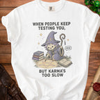 White t-shirt with a kawaii witch casting a spell saying "When people keep testing you, but karma's too slow."