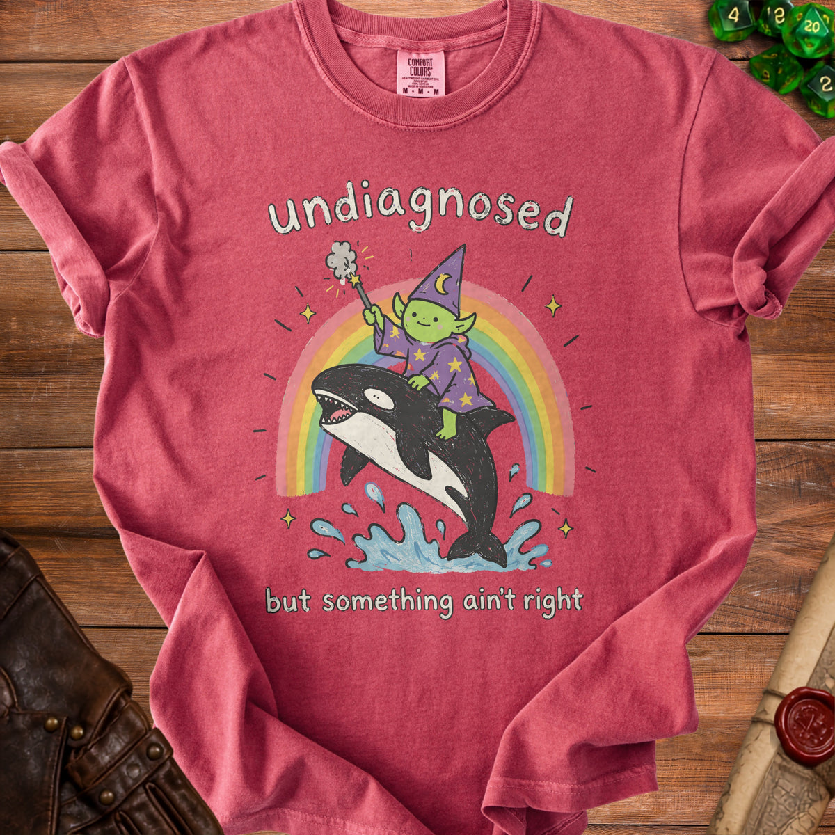 T-shirt graphic: green wizard rides killer whale over rainbow, text "undiagnosed but something ain't right".