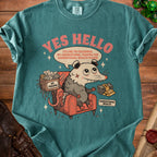 T-shirt graphic of a possum in a chair with the text "Yes Hello" and a speech bubble.