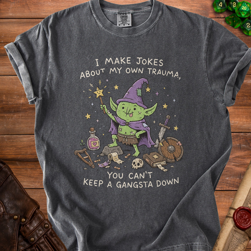 T-shirt with a cartoon goblin holding a wand and text "I MAKE JOKES ABOUT MY OWN TRAUMA, YOU CAN'T KEEP A GANGSTA DOWN".