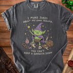 T-shirt with a cartoon goblin holding a wand and text "I MAKE JOKES ABOUT MY OWN TRAUMA, YOU CAN'T KEEP A GANGSTA DOWN".