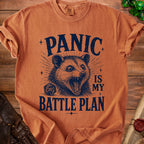 Orange t-shirt with dark blue graphic of a possum and text "PANIC IS MY BATTLE PLAN".