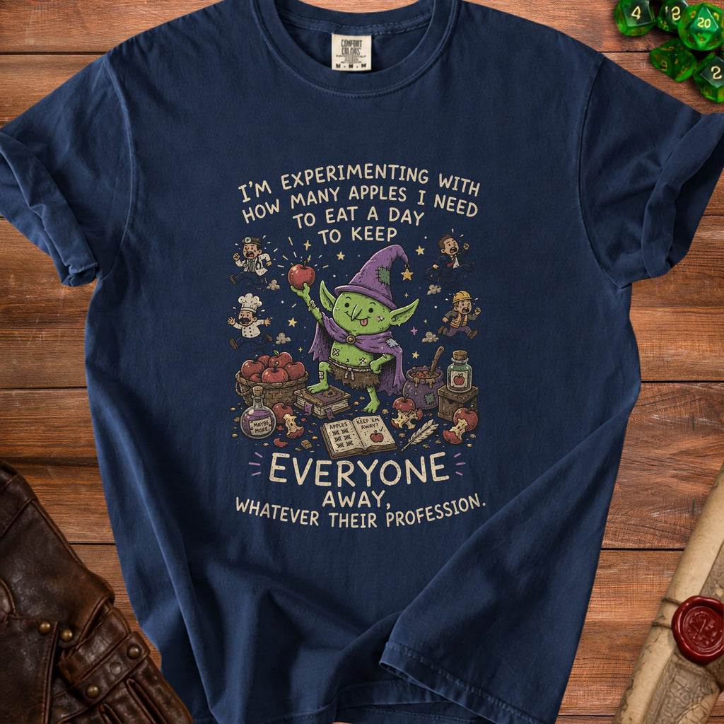 T-shirt graphic with a goblin holding an apple, text "I'm experimenting with how many apples I need to eat a day to keep everyone away."