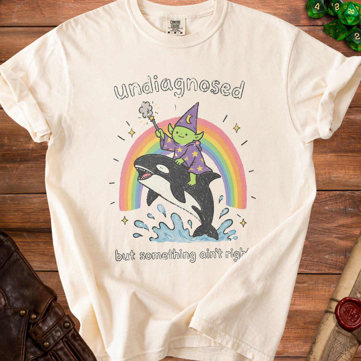 Cream t-shirt with illustration of a goblin wizard riding an orca over a rainbow.