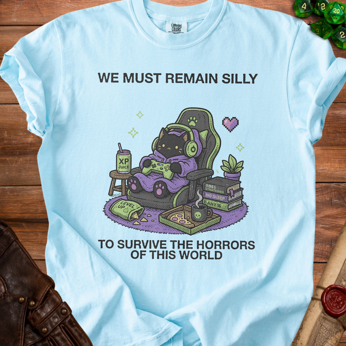 Light blue t-shirt with graphic of black cat gaming and text "WE MUST REMAIN SILLY TO SURVIVE THE HORRORS OF THIS WORLD".
