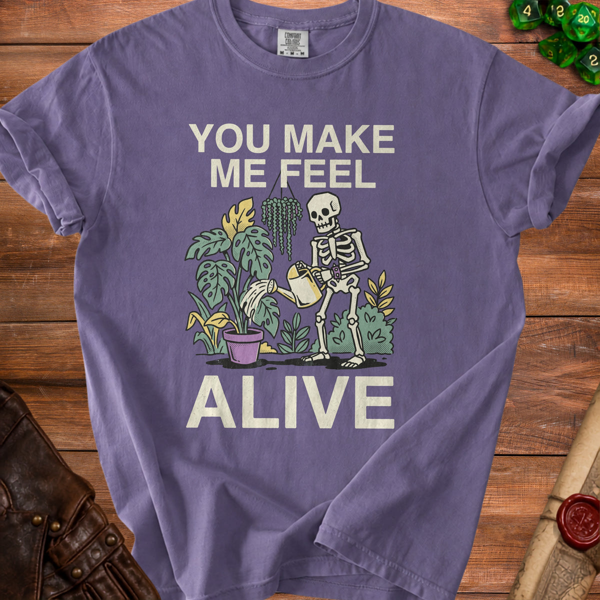 Purple t-shirt with a skeleton watering plants and text "YOU MAKE ME FEEL ALIVE".