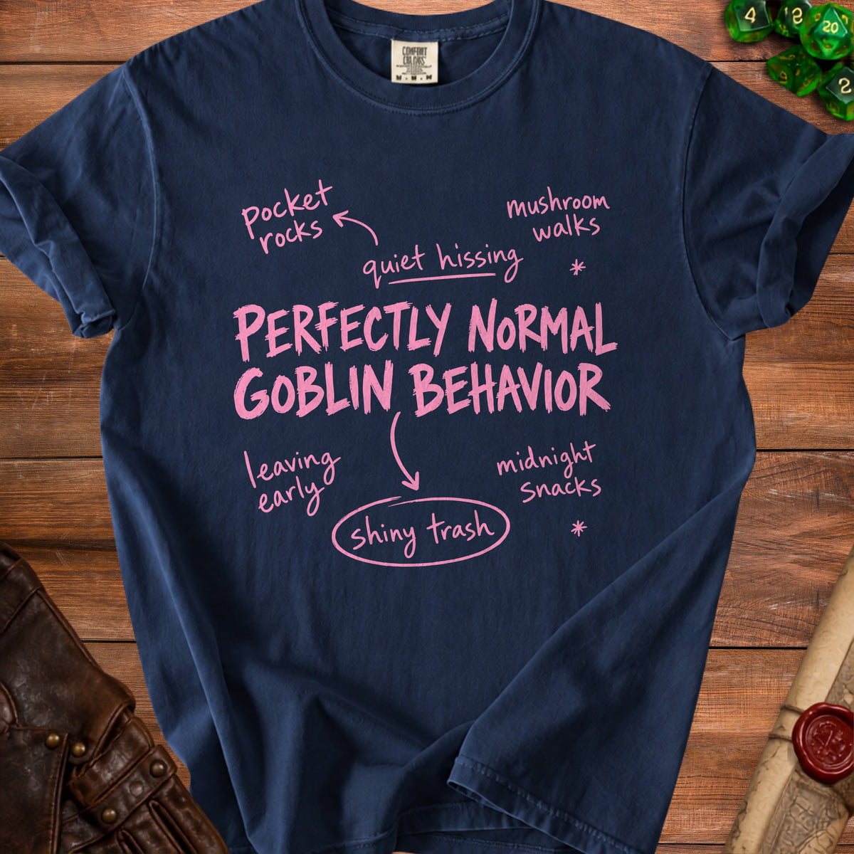 Navy blue t-shirt featuring pink text that reads Perfectly Normal Goblin Behavior surrounded by related phrases.