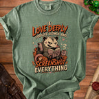 Green t-shirt with opossum graphic reading "I LOVE DEEPLY FORGIVE SLOWLY, AND SCREENSHOT EVERYTHING".