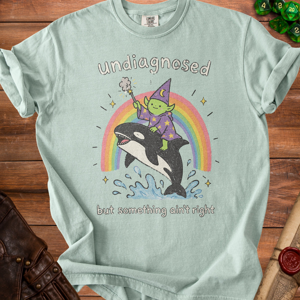 Light blue t-shirt with a graphic of a green goblin wizard riding an orca over a rainbow.