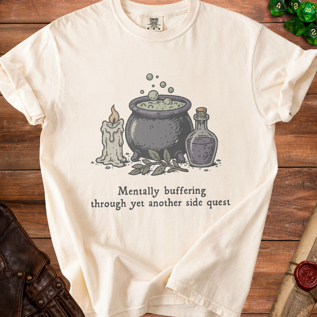 Cream t-shirt with cauldron, candle, potion, and text "Mentally buffering through yet another side quest".