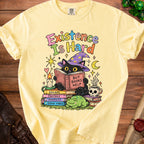 Yellow t-shirt with black cat wearing wizard hat reading a book, "Existence Is Hard But Books Help".