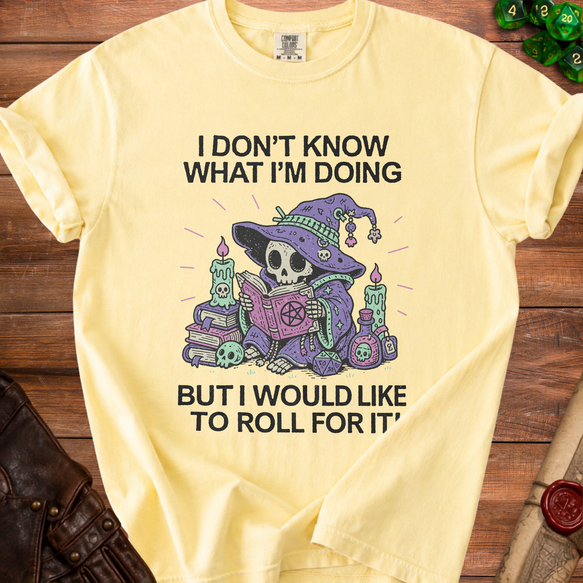Light yellow t-shirt with a skeleton wizard reading a book and dice.