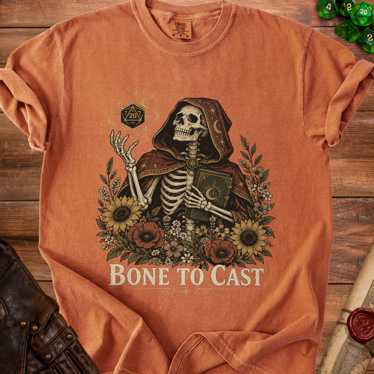 Skeleton wearing a hooded robe holding a book, surrounded by flowers and dice.