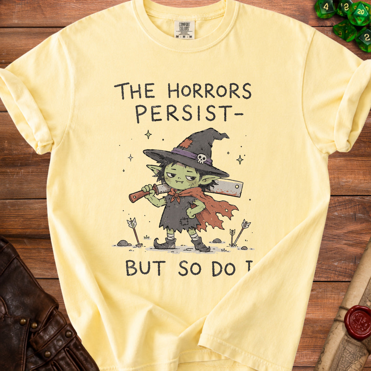 Yellow t-shirt with a goblin witch holding a cleaver and text "The Horrors Persist- But So Do T".