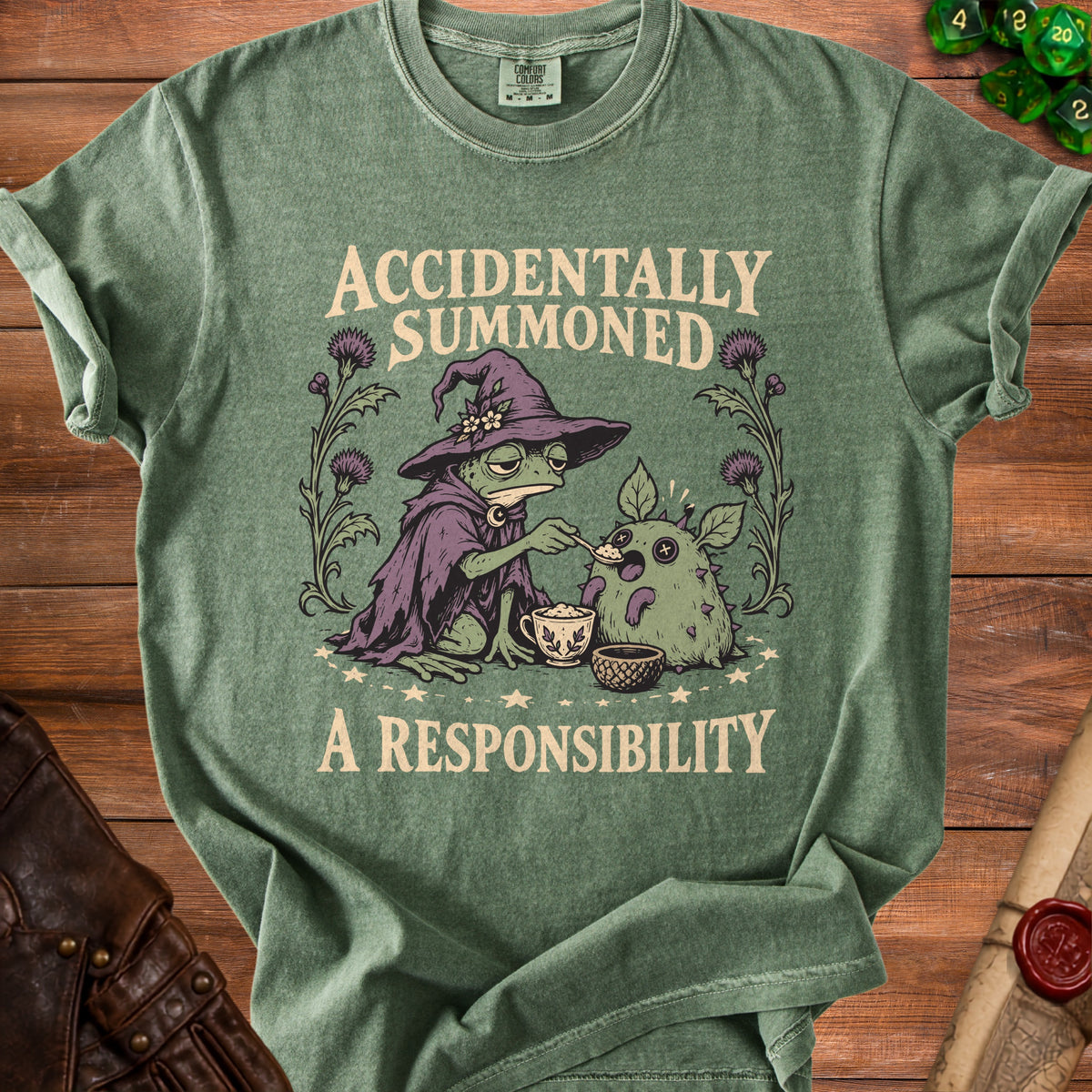 T-shirt graphic of a wizard frog feeding a creature, with text "ACCIDENTALLY SUMMONED A RESPONSIBILITY".
