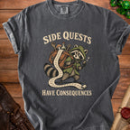 T-shirt with raccoon character carrying a long scroll, text "SIDE QUESTS HAVE CONSEQUENCES".