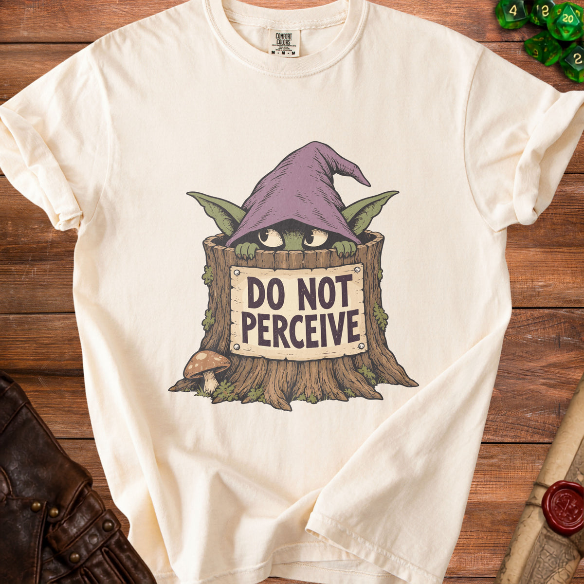 Cream t-shirt featuring a graphic of a green creature in a wizard hat hiding inside a tree stump with a sign that reads DO NOT PERCEIVE.