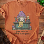 Orange t-shirt with a cartoon mushroom reading a scroll. Text reads "just here to avoid side quests."