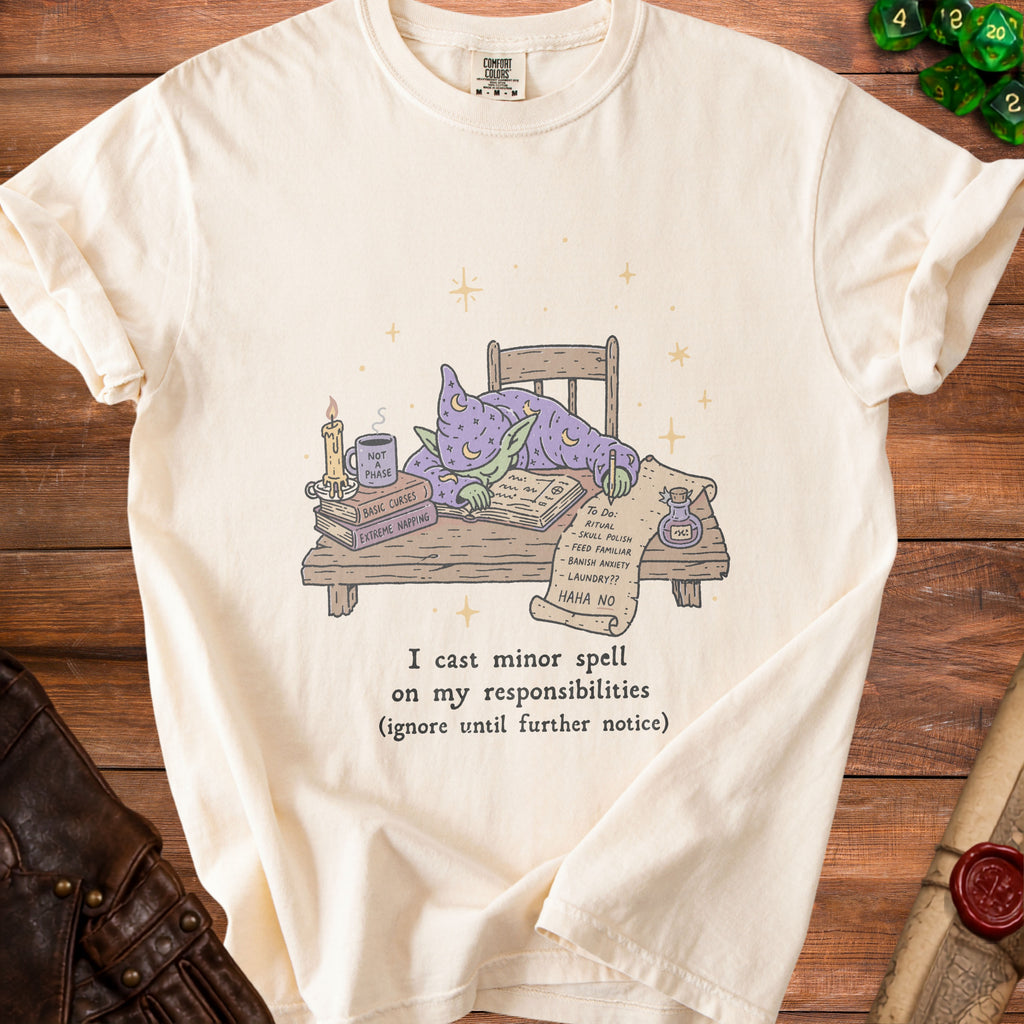 Cream t-shirt with a goblin in wizard robes sleeping at a desk with spellbooks and a to-do list.