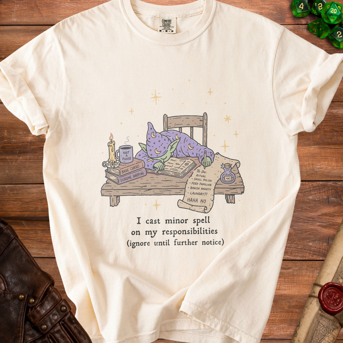 Cream t-shirt with a goblin in wizard robes sleeping at a desk with spellbooks and a to-do list.