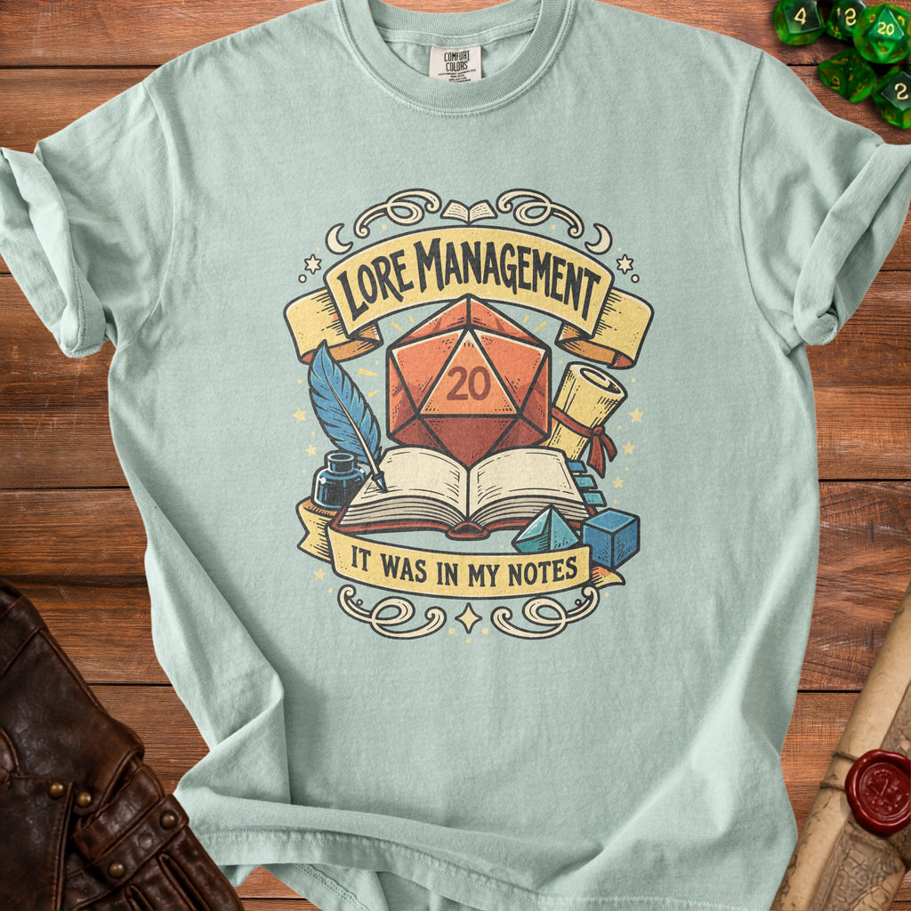 Light blue t-shirt with "Lore Management" and "It Was In My Notes" text and D20 die graphic.