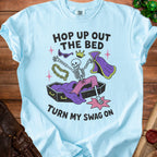 Light blue t-shirt graphic with skeleton in coffin, crown, sunglasses, and cape, text "Hop Up Out The Bed Turn My Swag On".