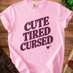 Pink t-shirt with "CUTE TIRED CURSED" text and heart design.