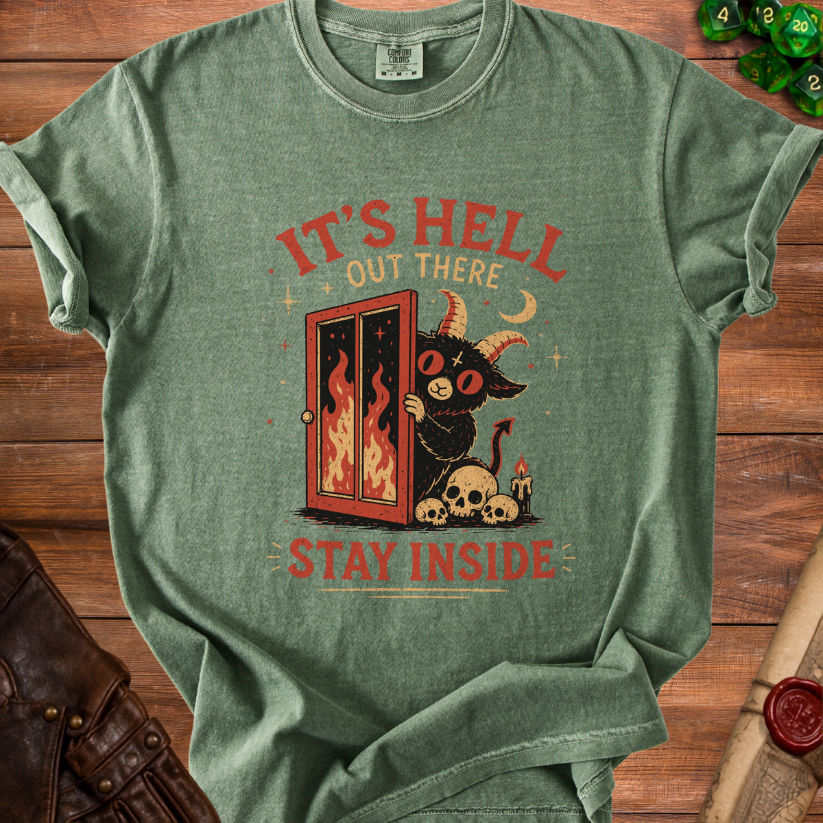 Green t-shirt with a devil peeking from a fiery doorway and text "It's Hell Out There Stay Inside".