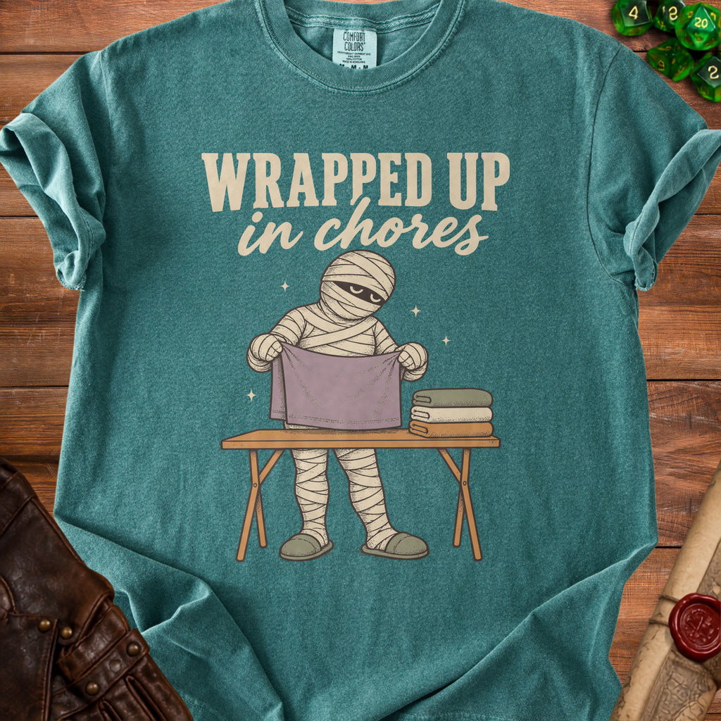 T-shirt graphic of a mummy ironing laundry with text "Wrapped Up in Chores".