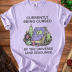 Light purple t-shirt with "Currently Being Cursed By The Universe (And Deadlines)" text and wizard graphic.