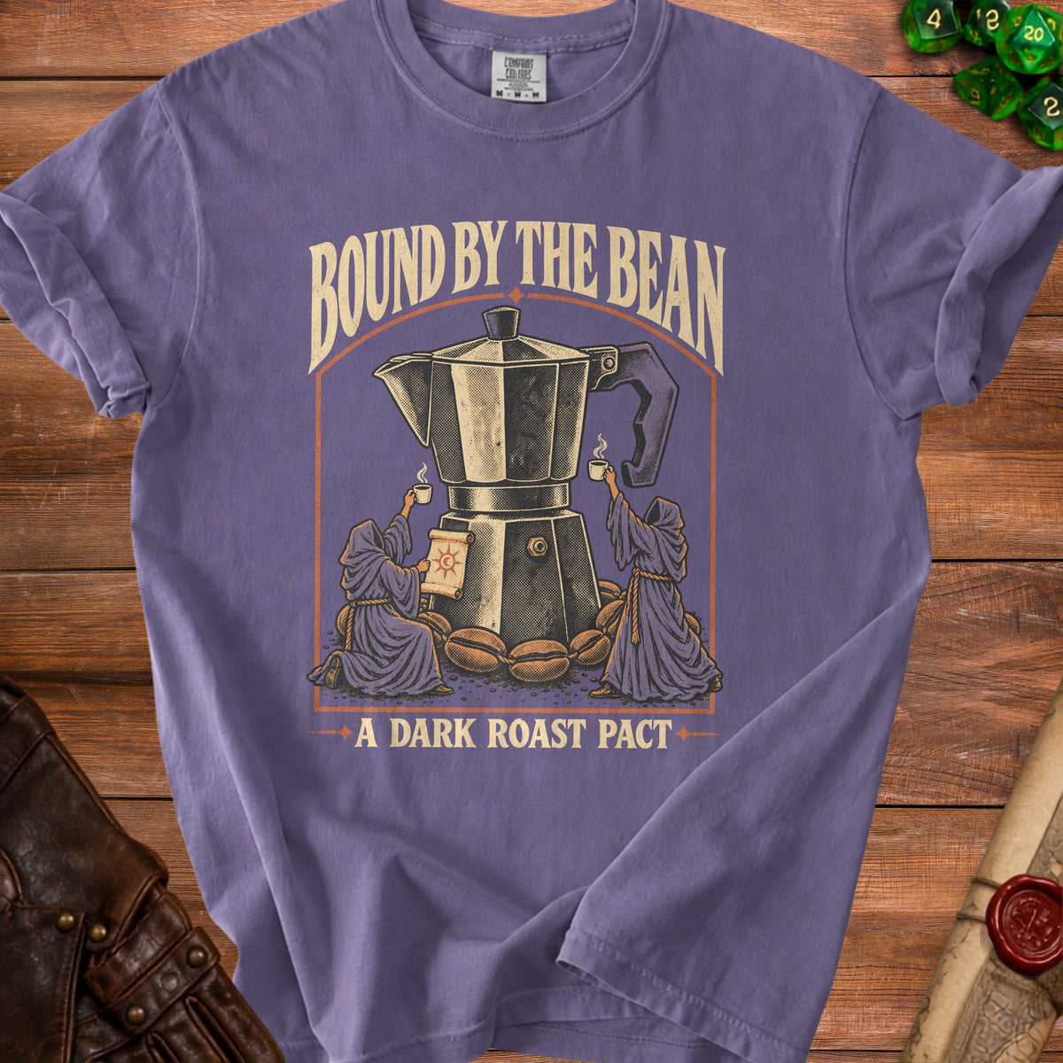 Purple t-shirt graphic with a moka pot, coffee beans, robed figures, and text "Bound By The Bean" and "A Dark Roast Pact".