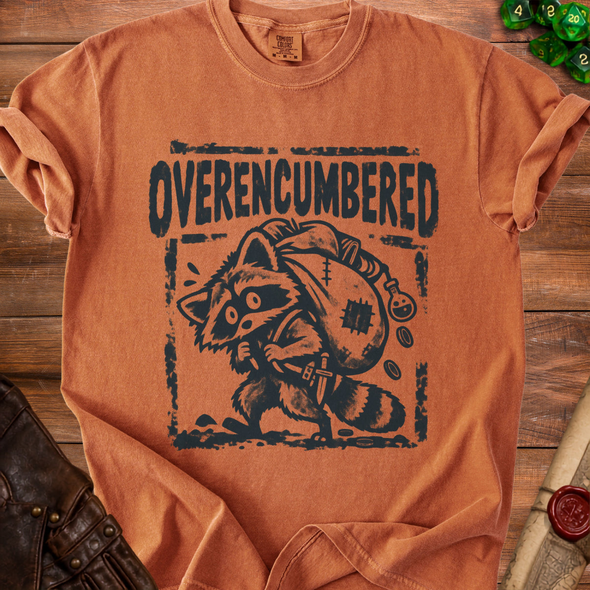 T-shirt with black graphic of a raccoon carrying a sack, with "OVERENCUMBERED" text.