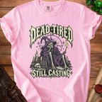 Pink t-shirt with skull in wizard hat and text "DEAD TIRED STILL CASTING".
