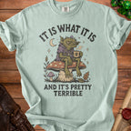 Mint t-shirt with graphic of a goblin on a mushroom, holding a skull mug. Text reads "IT IS WHAT IT IS AND IT'S PRETTY TERRIBLE".
