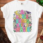 A white t-shirt with a colorful, whimsical graphic reading "A Little Chaos A Lot Of Magic" surrounded by celestial and magical icons.