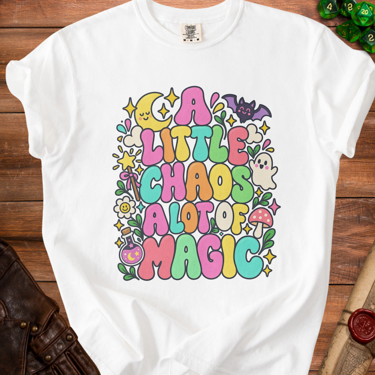 A white t-shirt with a colorful, whimsical graphic reading "A Little Chaos A Lot Of Magic" surrounded by celestial and magical icons.