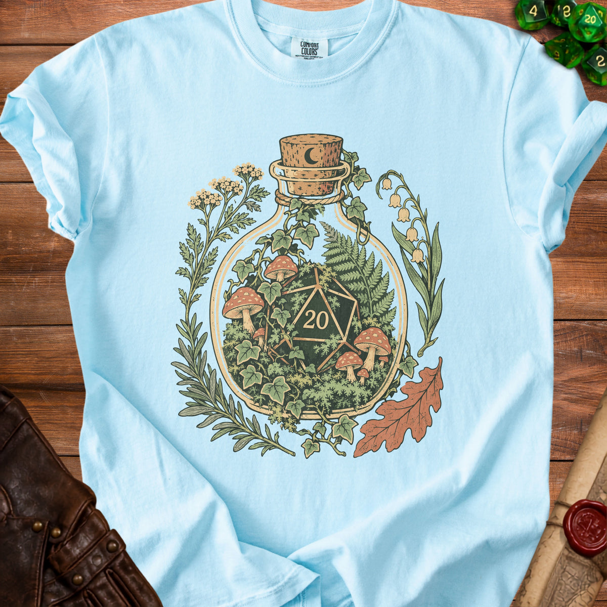 Light blue t-shirt with a glass bottle graphic containing a d20 die and mushrooms.