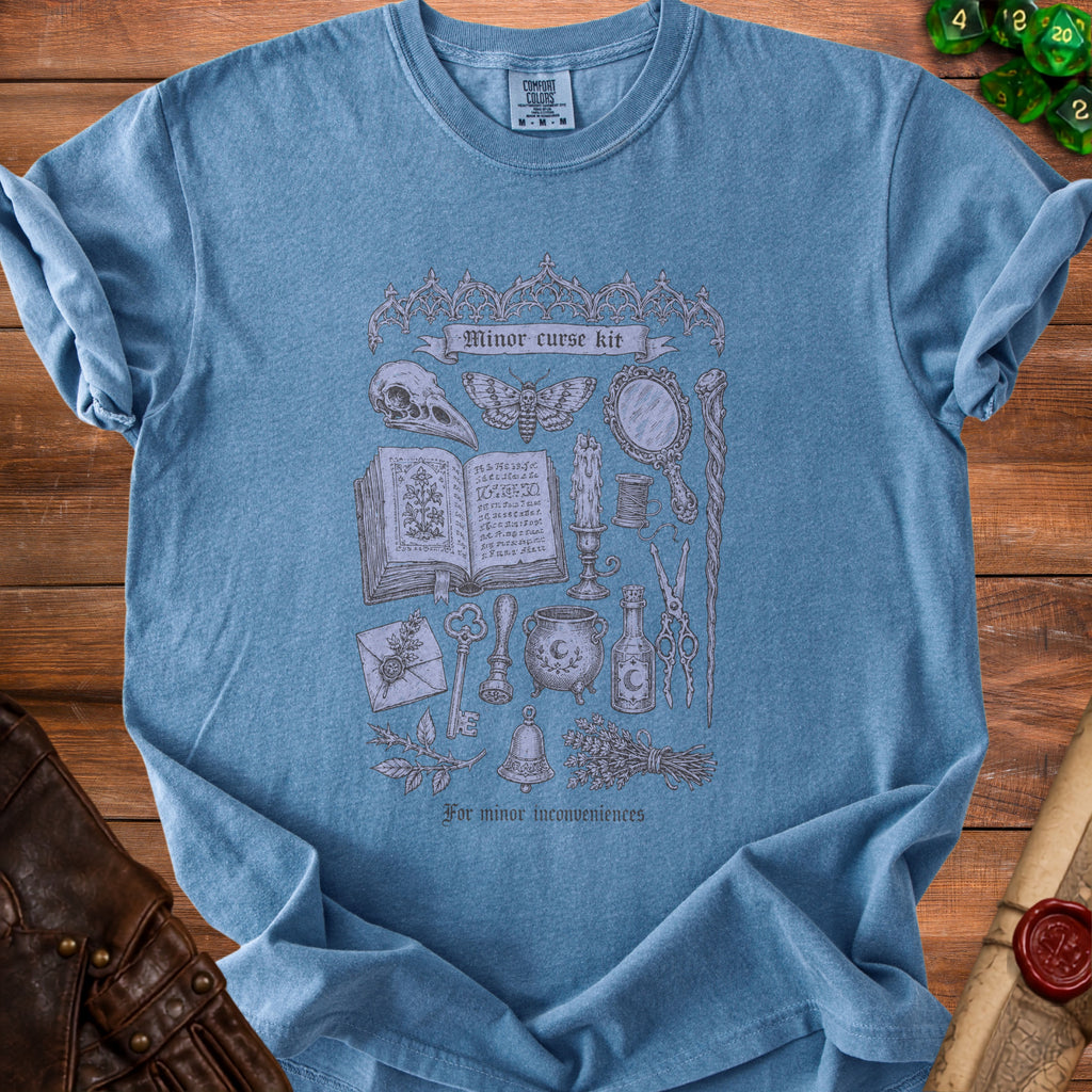Blue t-shirt with "Minor curse kit" design featuring occult imagery and "For minor inconveniences."
