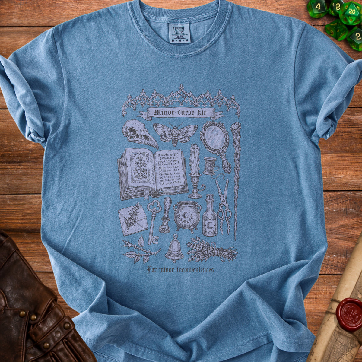 Blue t-shirt with "Minor curse kit" design featuring occult imagery and "For minor inconveniences."