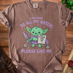 Brown t-shirt with a sad green goblin holding a sword and sign saying "Please Like Me".