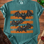 Teal t-shirt with three distressed black bats on orange and teal stripes.
