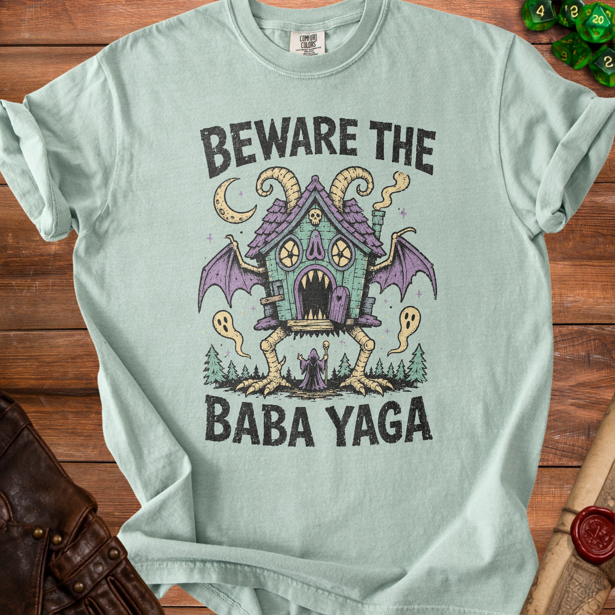 Light blue t-shirt with a graphic featuring a spooky house on chicken legs and the text "BEWARE THE BABA YAGA".
